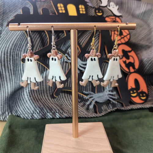 White ghost with pink cowboy hat and tan cowboy boots dangle earrings on a gold display stand with Halloween backdrop