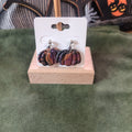 Dark marble clay pumpkin dangle earrings in deep purple, black, and terracotta on a wooden earring card stand