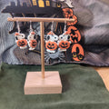 Large white spotted dog holding a jack-o'-lantern dangle earrings with orange bow on a gold display stand