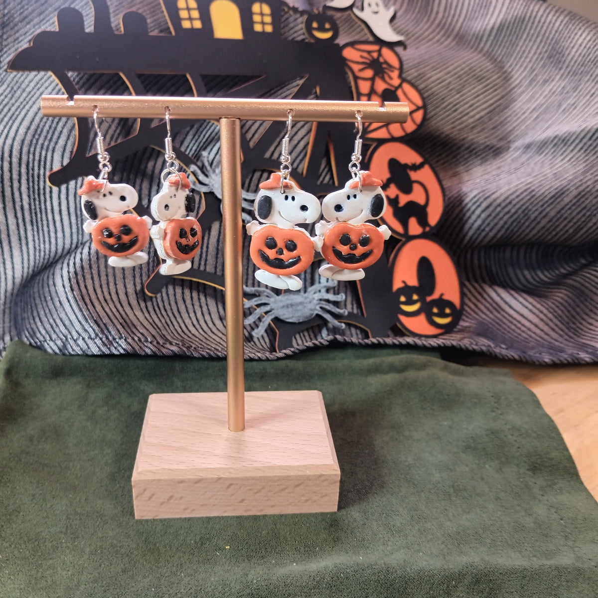 Large white spotted dog holding a jack-o'-lantern dangle earrings with orange bow on a gold display stand