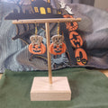 Tan puppy peeking out of an orange jack-o'-lantern dangle earrings on a gold display stand with Halloween backdrop