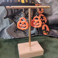 Orange jack-o'-lantern cutout hoop earrings with silver pavé leverback hooks on a gold display stand