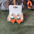 White goose in orange pumpkin costume dangle earrings displayed on a wooden earring card stand