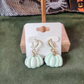 Mint green pumpkin dangle earrings with gold shepherd's hook ear wires on a wooden earring card stand