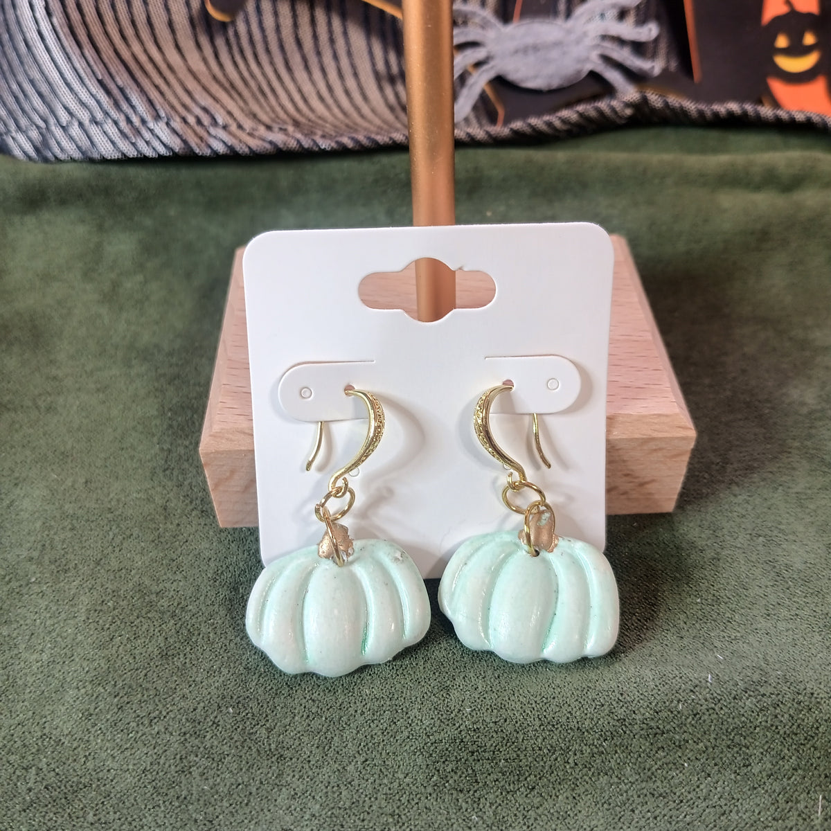 Mint green pumpkin dangle earrings with gold shepherd's hook ear wires on a wooden earring card stand
