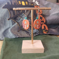 Orange pumpkin cottage dangle earrings with teal stem and purple floral details on a gold display stand