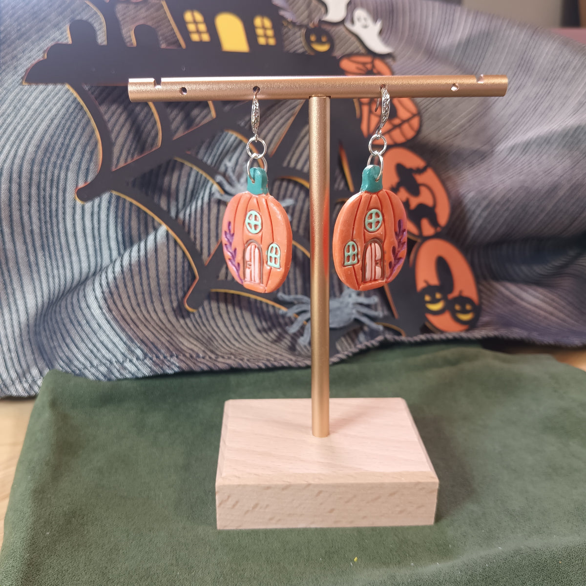 Orange pumpkin cottage dangle earrings with teal stem and purple floral details on a gold display stand