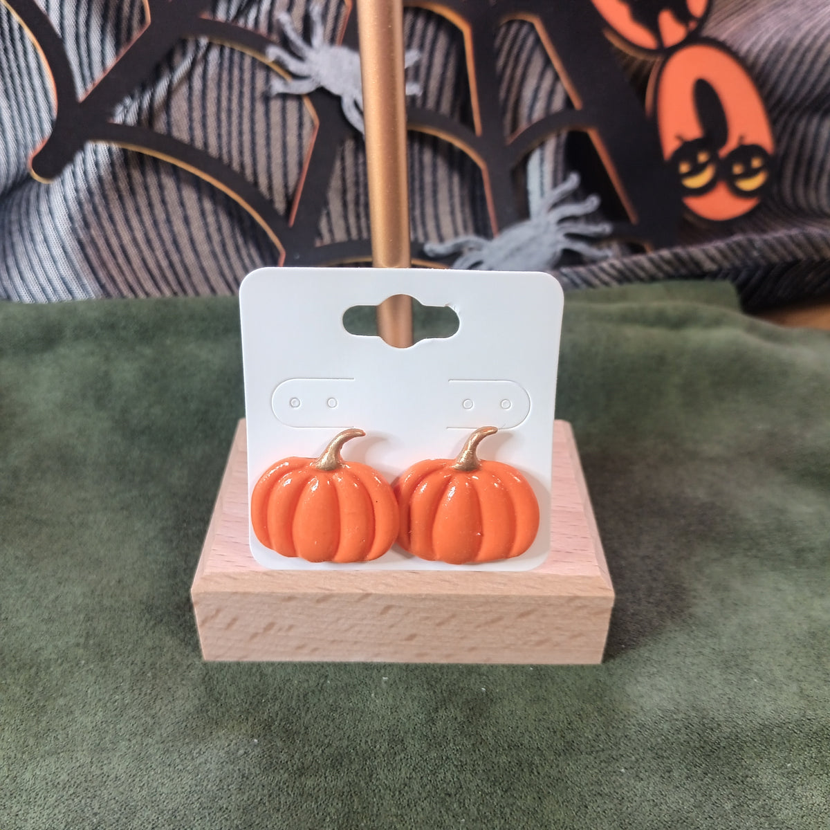 Orange pumpkin stud earrings with gold stem on a wooden earring card stand