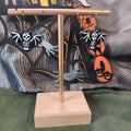 Skeleton bat dangle earrings hanging on a gold display stand with Halloween backdrop