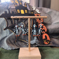 Skeleton penguin dangle earrings hanging on a gold display stand with Halloween backdrop