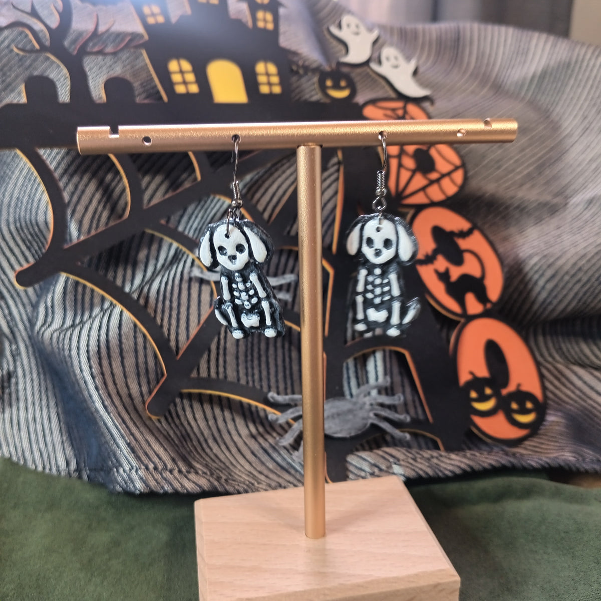 Skeleton dog dangle earrings hanging on a gold display stand with Halloween backdrop