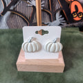 White pumpkin stud earrings on a wooden display stand