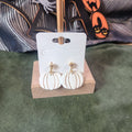 White and gold pumpkin dangle earrings on a wooden display stand