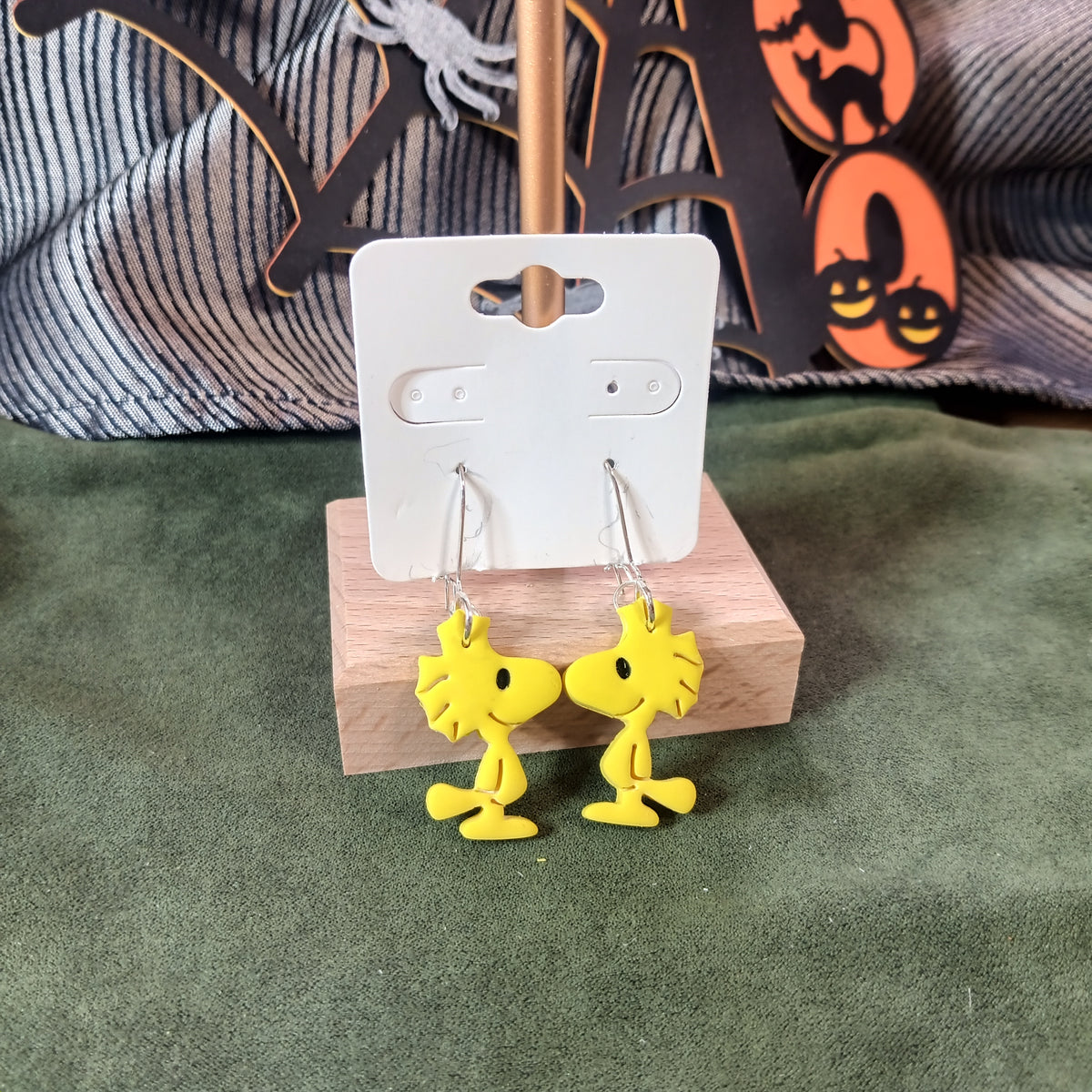 Yellow bird dangle earrings on a wooden display stand